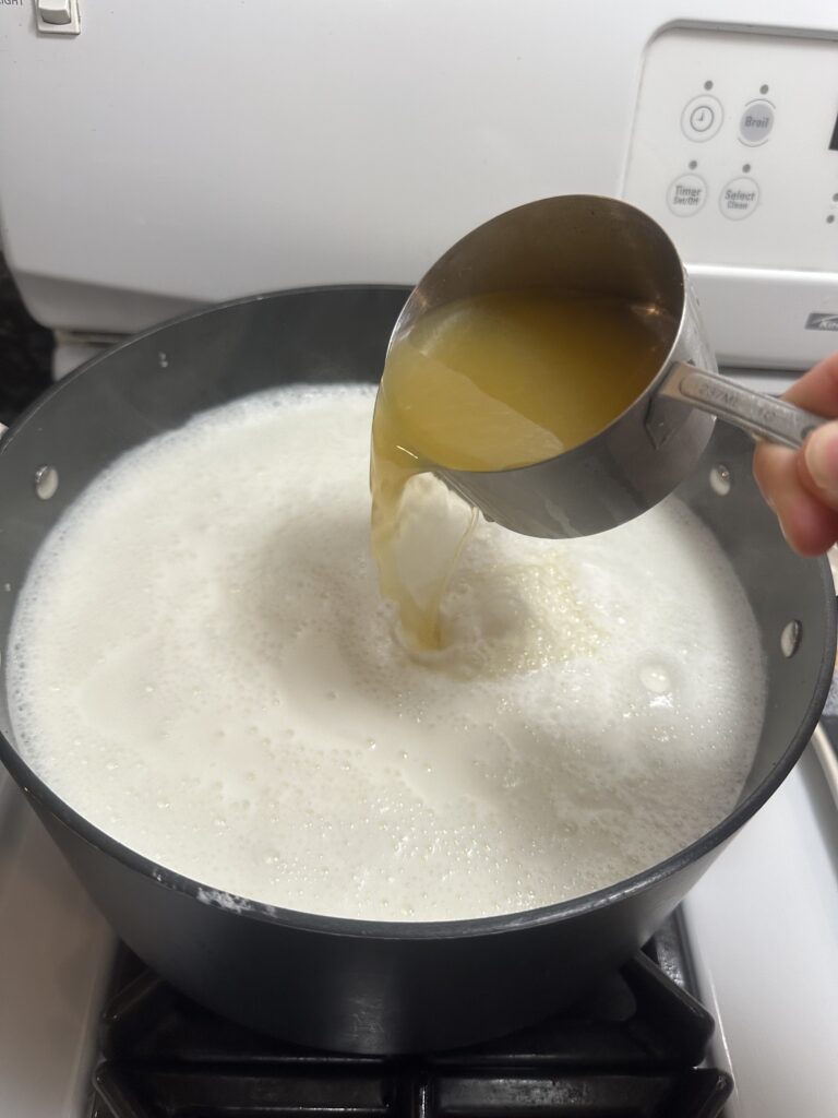 pouring in lemon juice into the warm milk to make cottage cheese