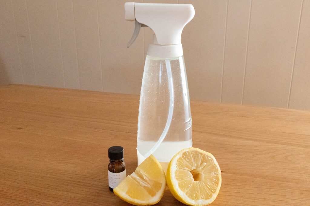 glass spray bottle holding an all-purpose spray and cut lemon in front of it