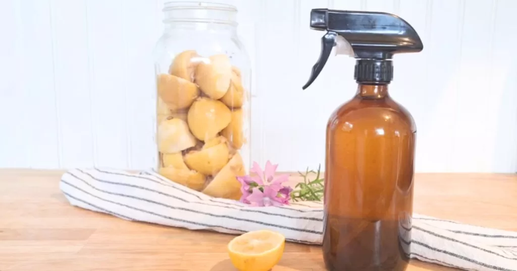 amber spray bottle with lemon peels, flowers, and tea towel in the background